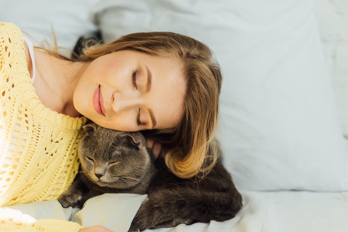 Femme aux yeux fermés recroquevillé avec un chat endormi sur le lit. statistiques de chat